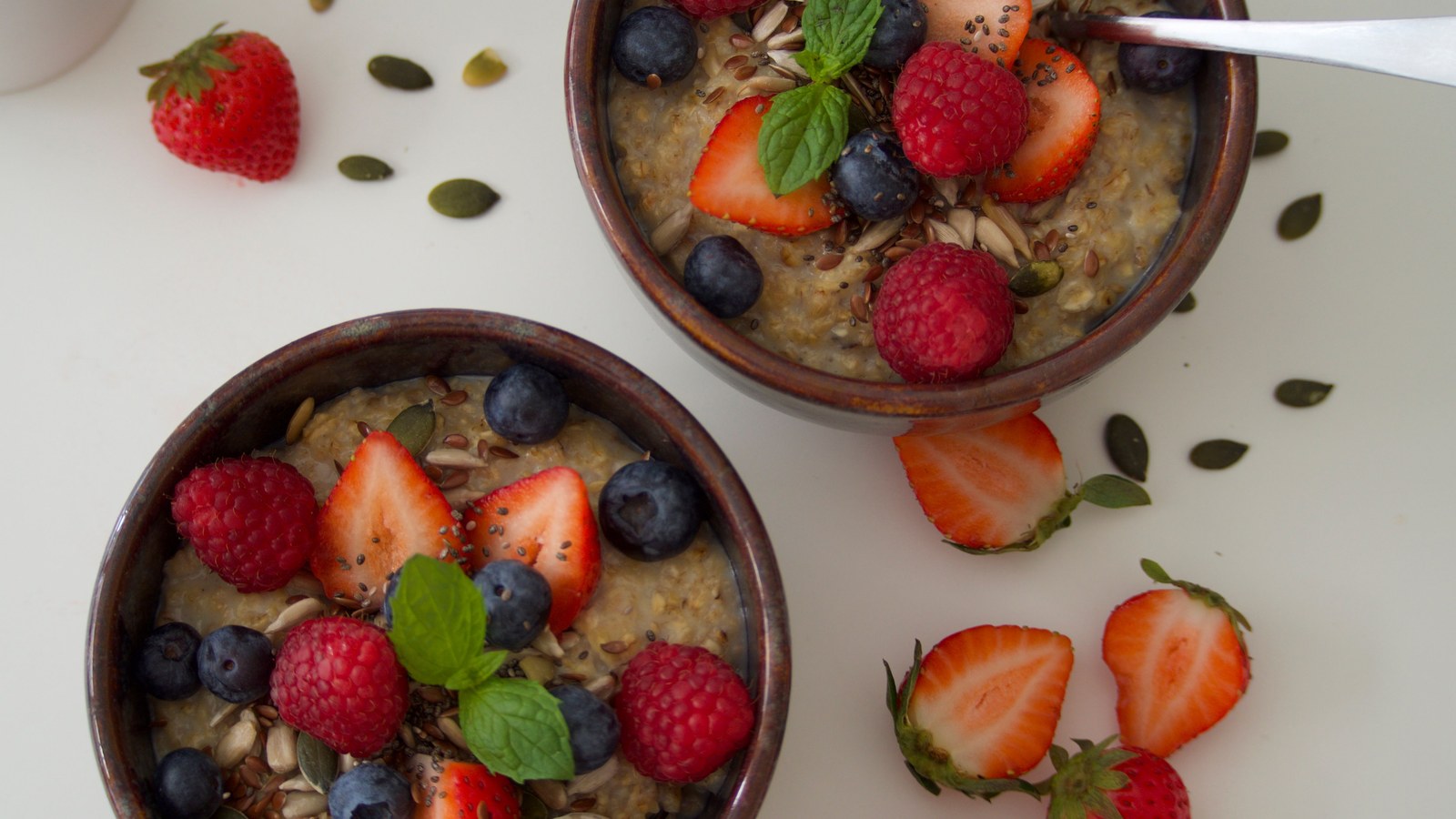 Two bowls of fibre-rich oatmeal topped with berries and seeds, representing a high-fibre diet for digestive regularity