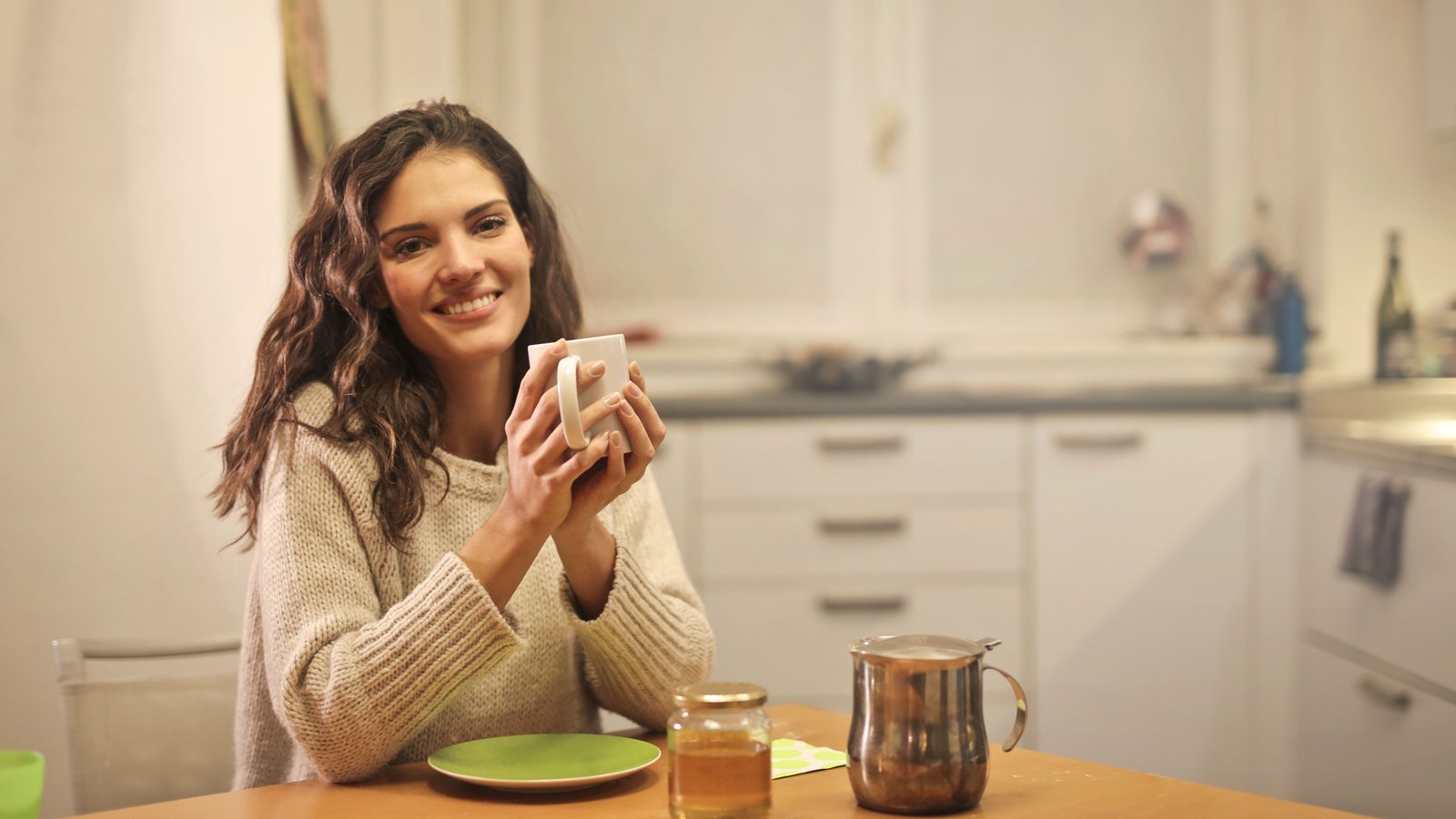 Wanita tersenyum sambil memegang minuman hangat di meja dapur, mewakili rutin pagi orang Malaysia