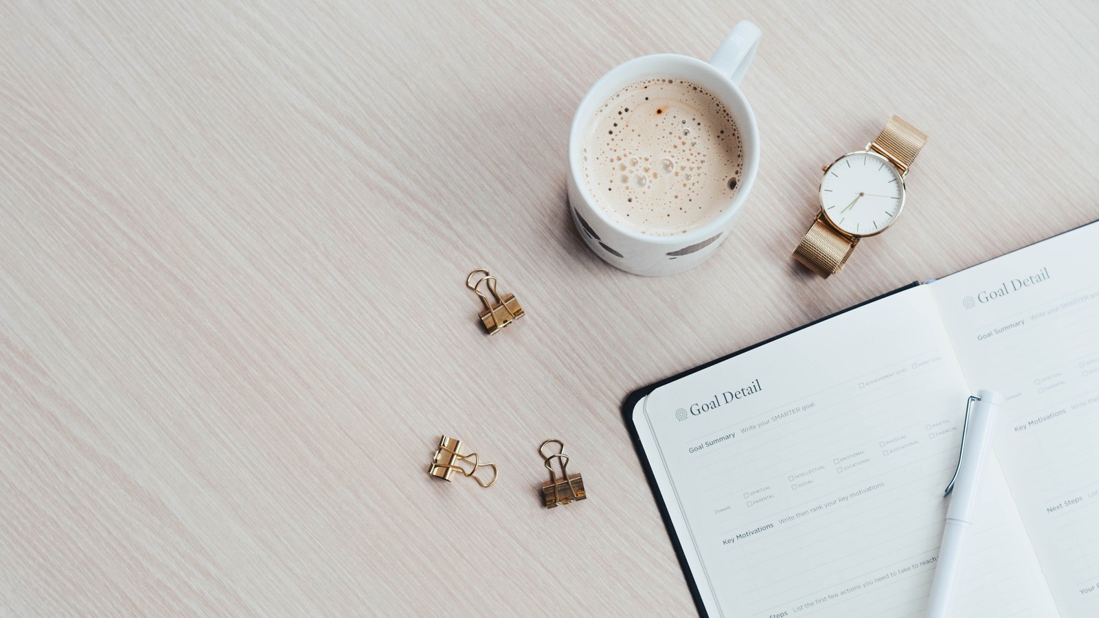 Flat lay of a coffee cup, watch, and goal-planning journal, representing a daily routine