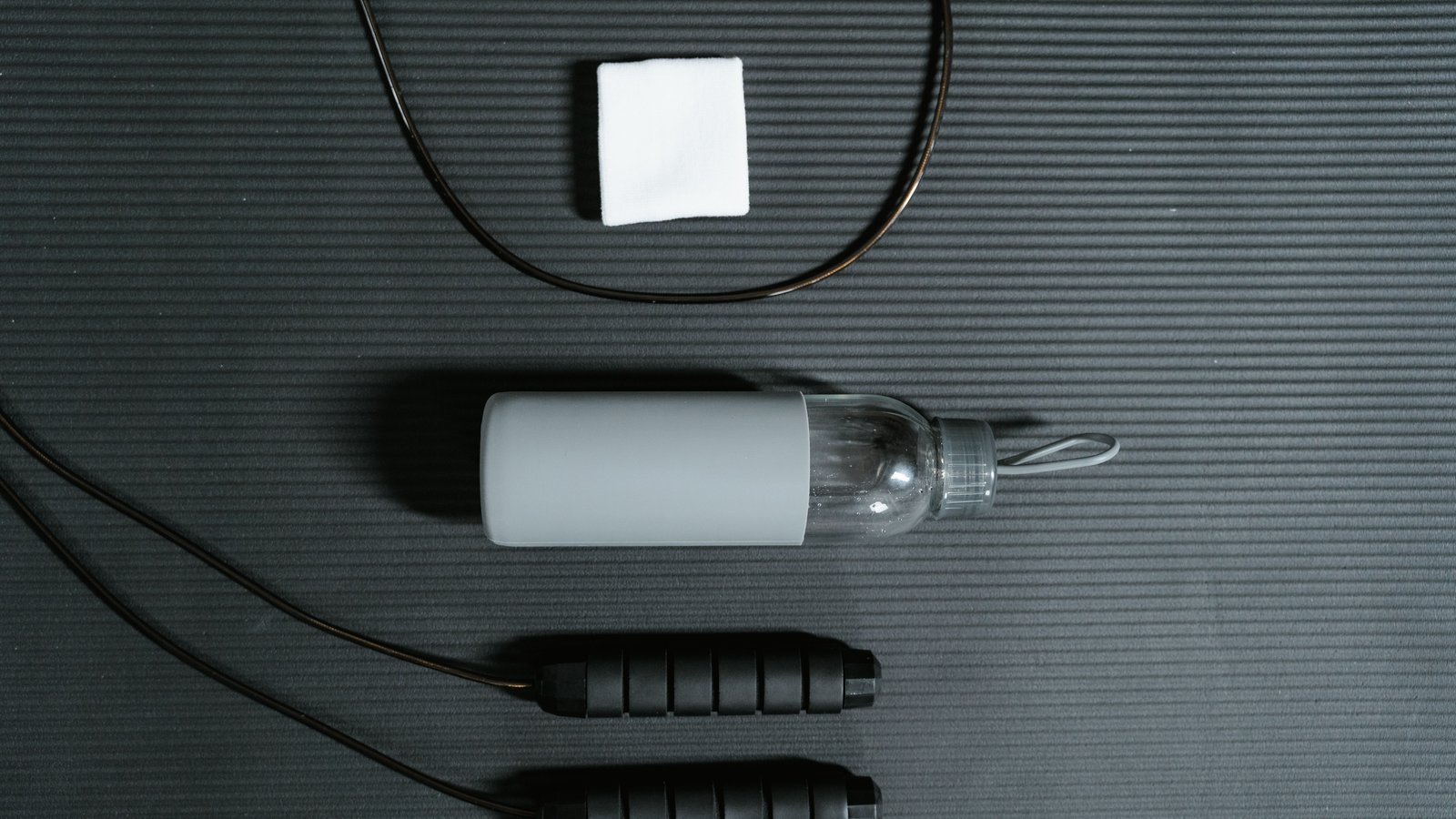A water bottle, towel, and jump rope laid out on a gym mat, representing a post-workout recovery routine