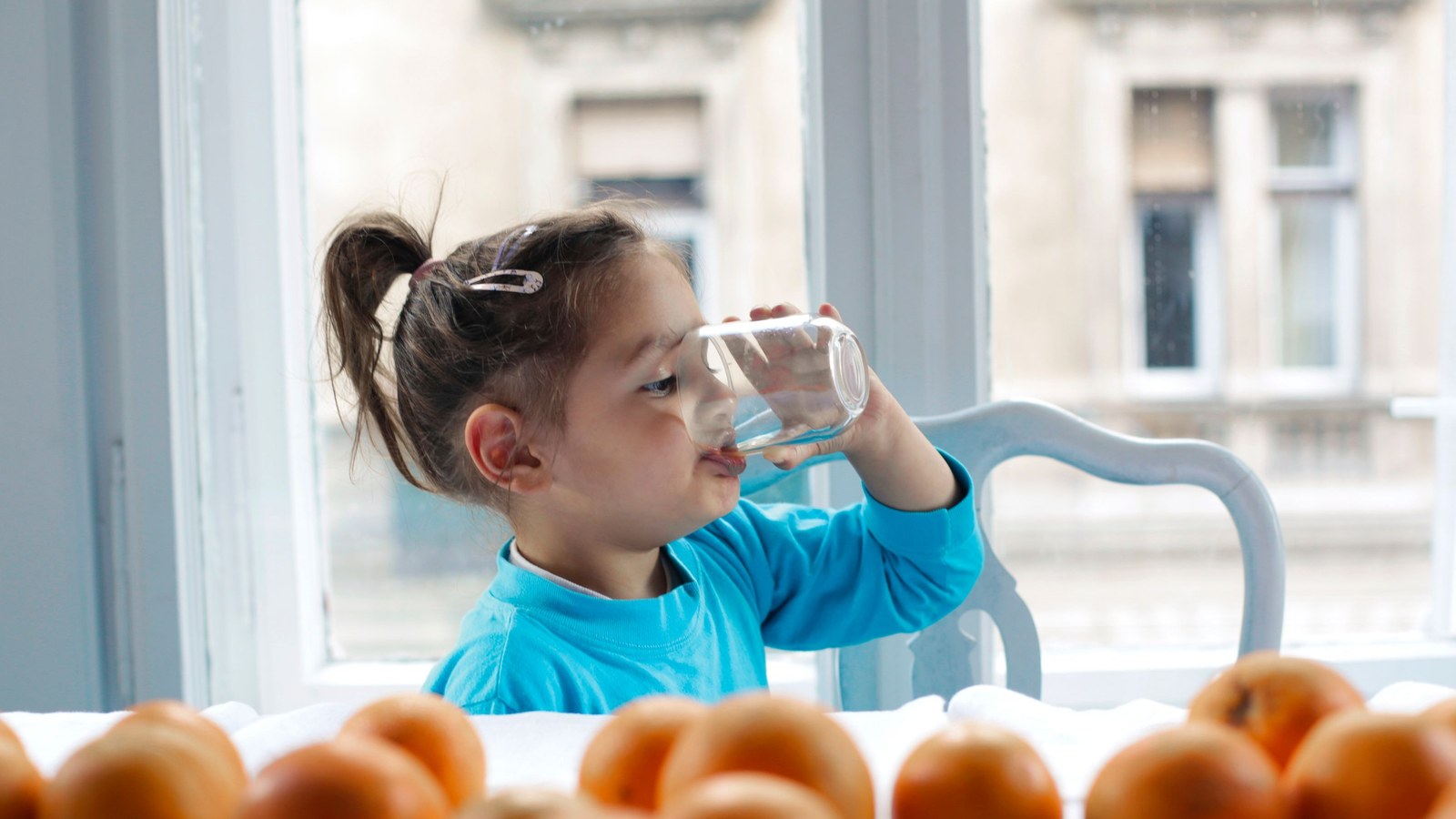 Young child drinking a glass of water at a table, representing questions about giving Arabic gum to kids