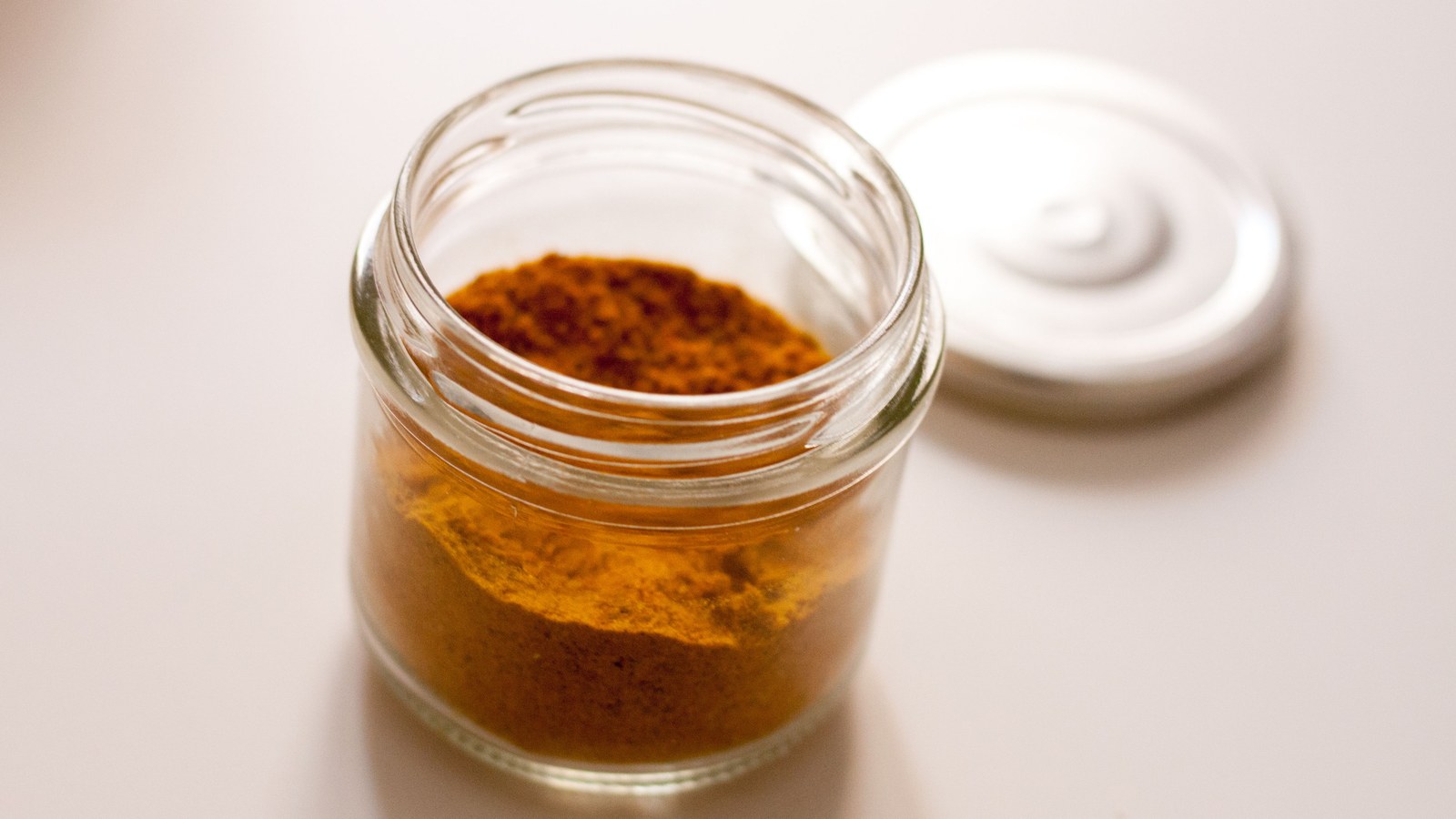 Powder stored in an open glass jar with its lid beside it, representing proper airtight storage for Arabic gum powder