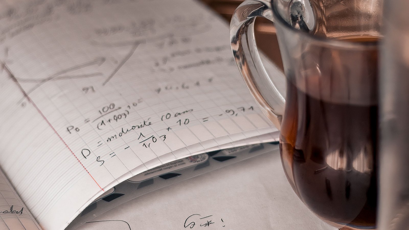 A study notebook covered in handwritten notes and equations, next to a warm drink, representing exam season